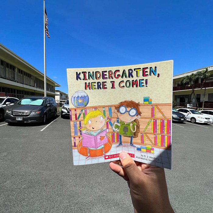 A hand holding a children's book with the inscription,'kindergarden, here I come!'